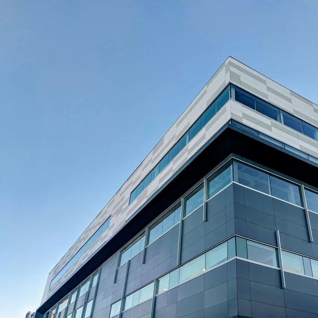 The upper corner of a modern glass-and-panel office building against a clear sky